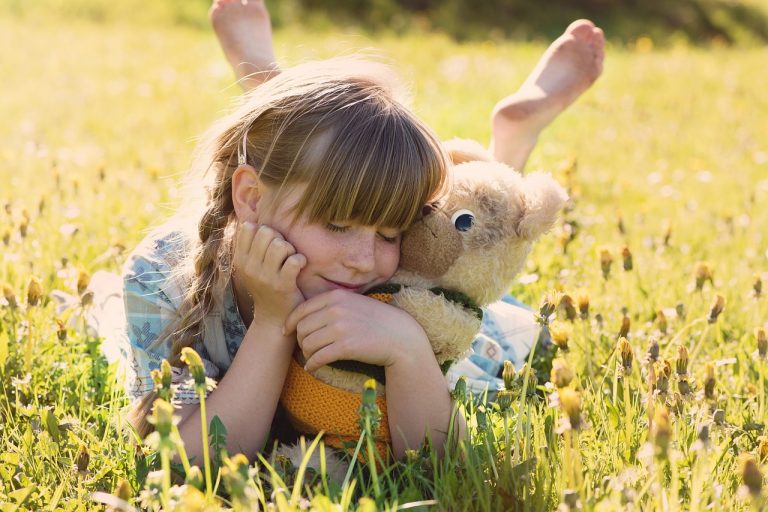 niña en el campo abrazando un oso de peluche día soleado
